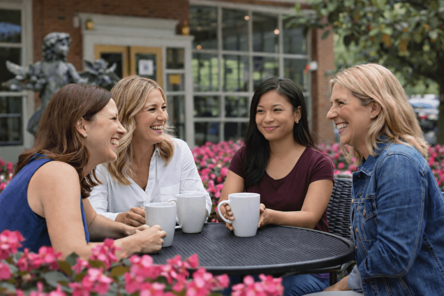 Four women enjoying coffee together at an outdoor cafe, representing the informal fellowship of ministry meetups