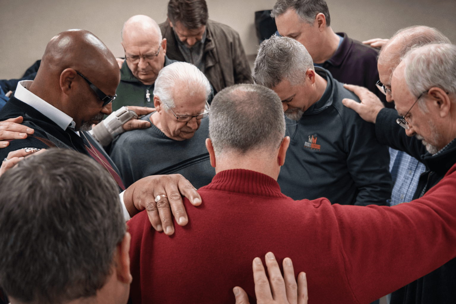 Diverse group of pastors and ministry leaders in a prayer circle with hands on each other's shoulders, representing fellowship and support